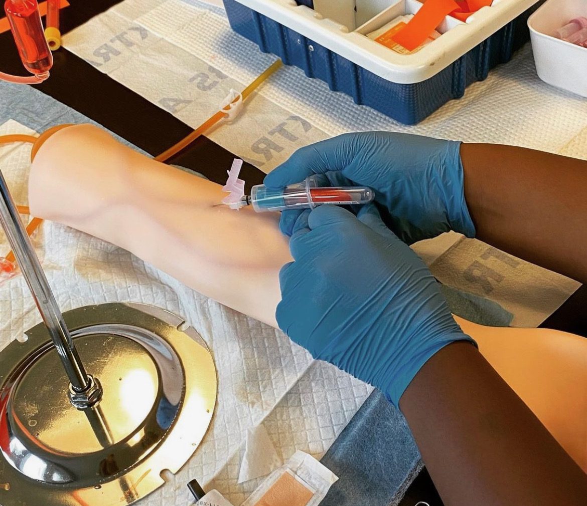 A phlebotomy student performing venipuncture on a training arm